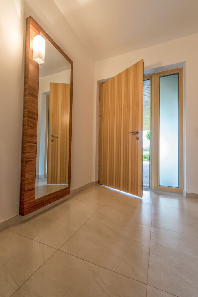 Eingangsbereich mit großem Spiegel und geöffneter Eingangstür aus Holz, mit Fixverglasung